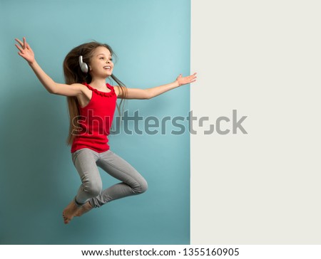 Little cheerful girl with long hair  in gray headphones listens to music, dances, jumps and has fun.