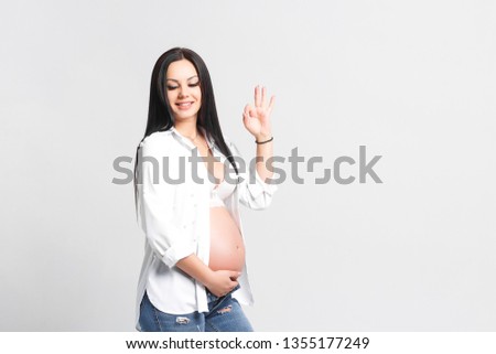 Young,brunette  pregnant woman isolated on white background turns on her finger. All things is okay! Health life!