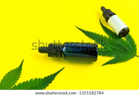 Hemp leafs and cannabis oil extracts in bottles on yellow background