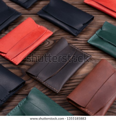 Flat lay photo of five different colour handmade leather one pocket cardholders.  Red, black, blown, ginger and green colors. Stock photo on wooden background. 