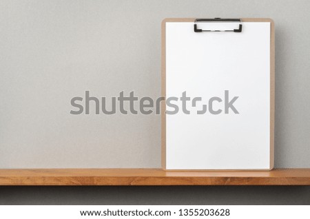 Design concept - front view of A4 paper with clipboard on bookshelf and grey wall for mockup, not 3D render
