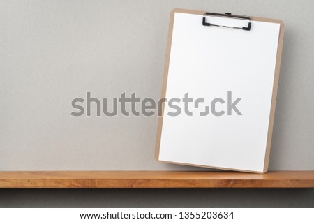 Design concept - front view of A4 paper with clipboard on bookshelf and grey wall for mockup, not 3D render