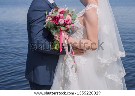 bride and groom stand together against the water