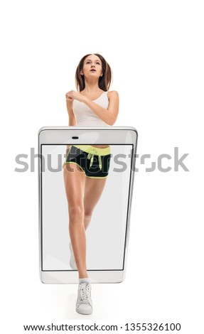 Portrait of young attractive slim fit woman jogging, concept virtual reality of the smartphone. going out of the device