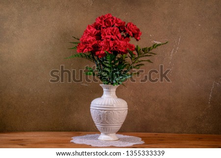 Dozen of red carnations in fine china vase on wooden oak table  and minimalistic brown and tan background for Easter holiday
 