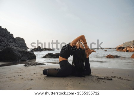 Young healthy woman practicing yoga on the beach at sunset.