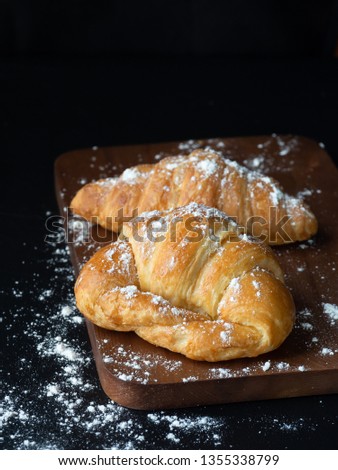 Croissant with icing on wood board in Chiaroscuro photo style, black background, Free space. 