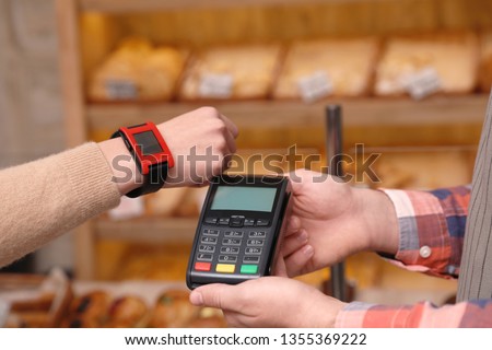 Woman using terminal for contactless payment with smartwatch in bakery, closeup