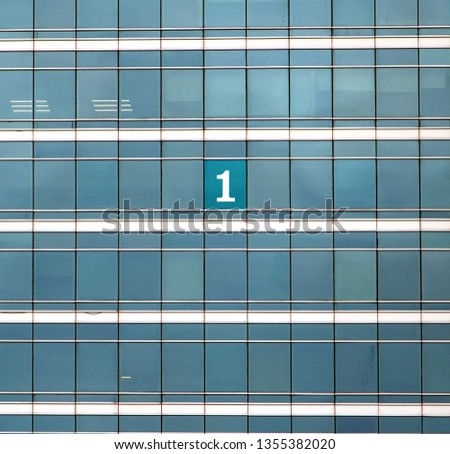 The mumber One on the building's window. The glass facade of skyscraper with many identical windows and one window with sign 1.