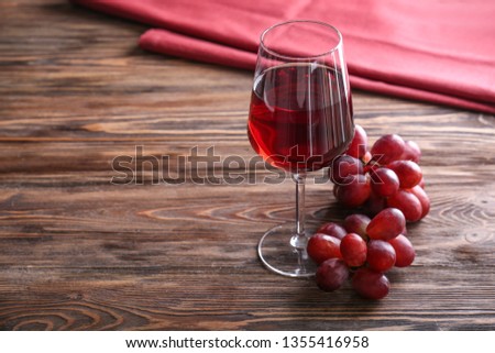 Glass of tasty wine with grapes on wooden table