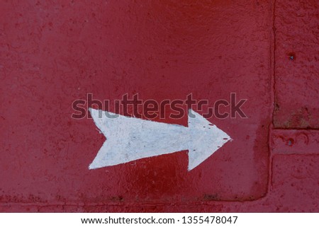 White arrow direction on red metal background on ship deck