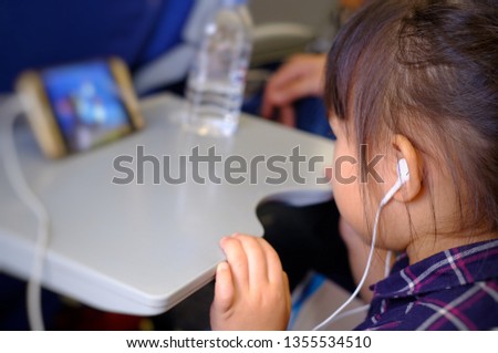 Asian little girl is wearing headphones to watch cartoons on the phone. While traveling on the airplane.