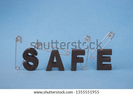 The word safe pierced by safety pins on a blue background