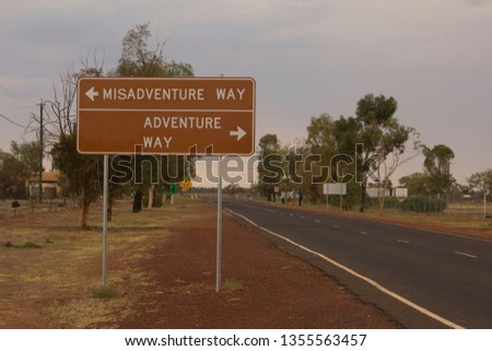 A road sign, changed to read Misadventure Way one way, adventure way the other, with an empty bitumen road running past