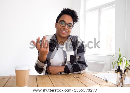 Head shot portrait of talking smiling African American woman wearing glasses, looking at camera, making video call, chatting with friends, blogger recording video, sharing thoughts, sitting at desk