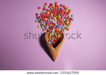 Ice cream waffle cone and scattering of multicolored sweets and confectionery topping on color background