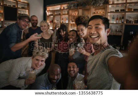 Laughing group of diverse young friends talking a selfie together while having a fun night out in a bar