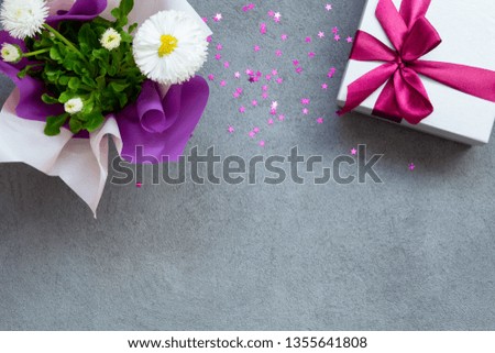 Gift box and daisy flowers on grey stone table, flower concept with copy space, top view