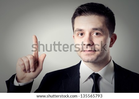 businessman holding a finger up on a gray background