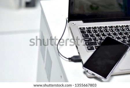 Open laptop and black smartphone. All with isolated screen on wooden table, selective focus.
