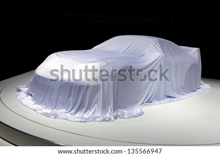 Covered car. Sport car covered with a white cloth in a exhibition on black background