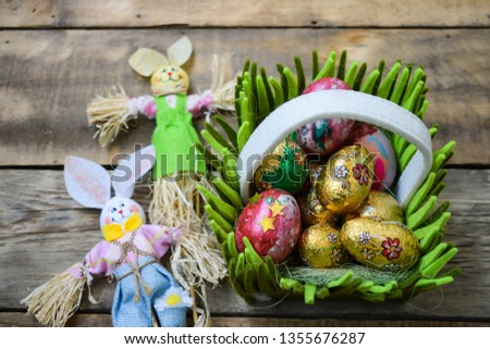 Golden and dyed Easter eggs in the basket framed with grass with cute Mr. and Mrs. Bunny on the wooden background, close up