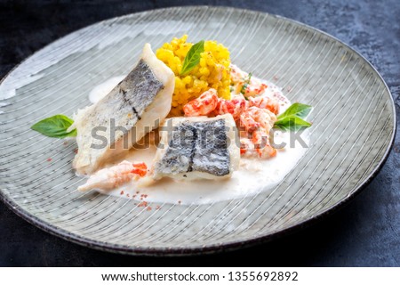 Fried haddock filet with saffron rice and shell prawns in crab sauce as closeup on a modern design plate 