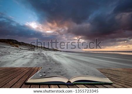Beautiful Winter sunrise over West Wittering beach in Sussex England with wind blowing sand across the beach in pages of open book, story telling concept