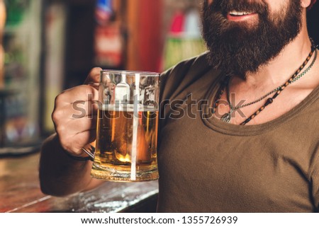 Cropped image of handsome bearded man is drinking beer in pub. Man enjoying good beer in night club. Party time, lifestyle, beer time