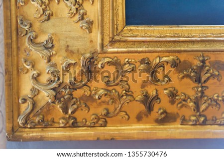 Texture carved wooden frame. An old painting in a gilded frame. The interior of the room. Decorative element.