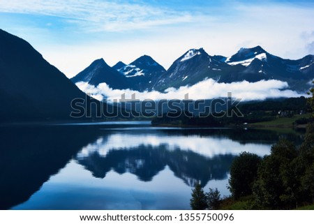 Blue landscape with snow-capped mountains and thier reflection in water