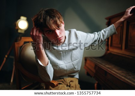 A man is sitting on a chair next to a spotlight and a piano