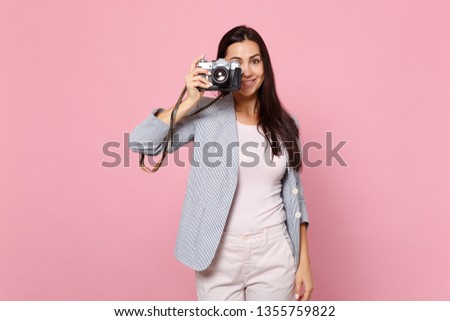 Portrait of charming young woman in striped jacket taking pictures on retro vintage photo camera isolated on pink pastel wall background. People sincere emotions lifestyle concept. Mock up copy space