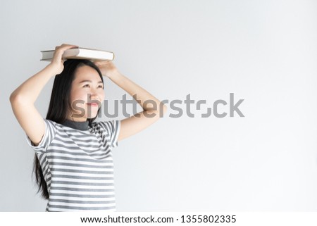 Asian woman student of university standing on a white background holding a book on women head. Women smiling be happy. Female is looking outside 