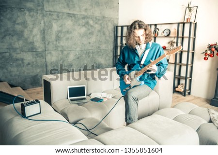 Personal creation. Artistic young man actively playing on guitar in the middle of the room while being at home alone