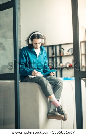 New composition. Chilling concentrated guy sitting on back of the couch with headphones on and filling personal album