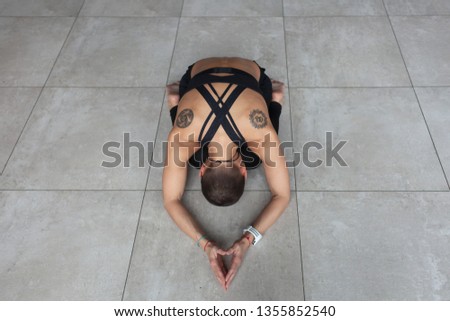young short hair woman with hinduism tattoos meditating in yoga child pose, balasana on stone floor
