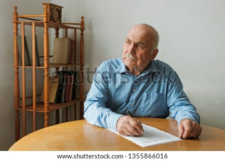 Old man writing notes or deciding whether to sign a paper document on the table in front of him as he looks to the side with a thoughtful engrossed expression Royalty-Free Stock Photo #1355866016
