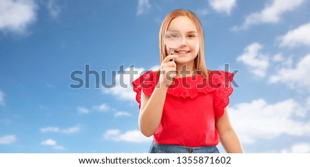 investigation, discovery and vision concept - happy girl looking through magnifying glass over blue sky and clouds background