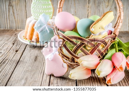 Easter holiday greetings background, basket with pastel colored eggs, Easter baking cupcake cookies, spring flowers. Wooden rustic background, copy space