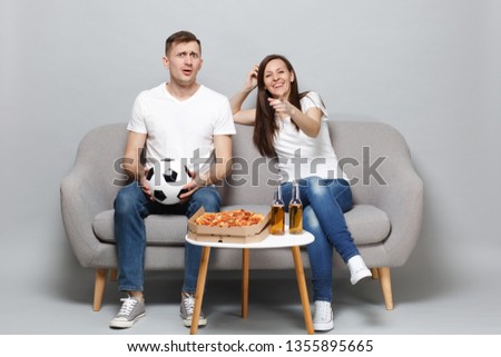 Fun couple woman man football fans cheer up support favorite team with soccer ball pointing index finger on camera isolated on grey background. People emotions, sport family leisure lifestyle concept