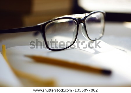 Glasses lying in the workplace, among a notebook, pencil and other items. The light falls on the glasses and is reflected in the stains on the glasses