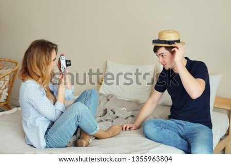 happy girl and guy take pictures of each other with old camera posing in straw bowler hat and smiling in bedroom