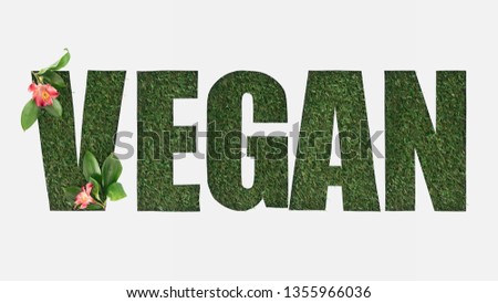 top view of cut out vegan lettering on green grass background with alstromeria flowers and leaves isolated on white