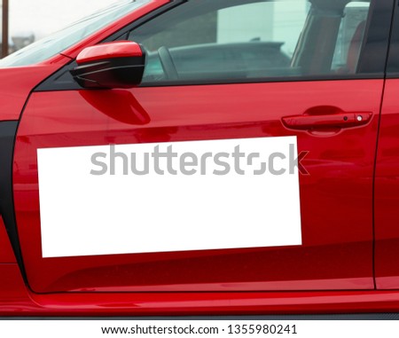 Horizontal shot of a blank white magnetic sign on a red car’s driver side door.