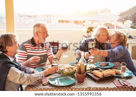 Happy senior friends dining and cheering with red wine at barbecue in terrace outdoor - Retired people having fun at bbq party on patio - Friendship, food and elderly lifestyle concept 
