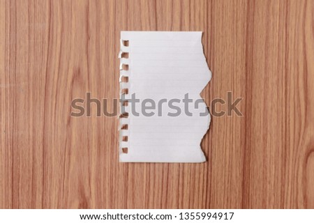 Sheet of notebook paper with torn edge blank ripped piece on isolated over wooden table background. Empty Damaged Rip Paper Shape. Clipping path, copy space room for text, educational design concept