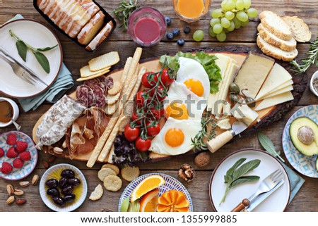  Brunch or breakfast set, meal variety with fried eggs, sausage and cheese variety, granola, smoothie, fruits and berries. Overhead view