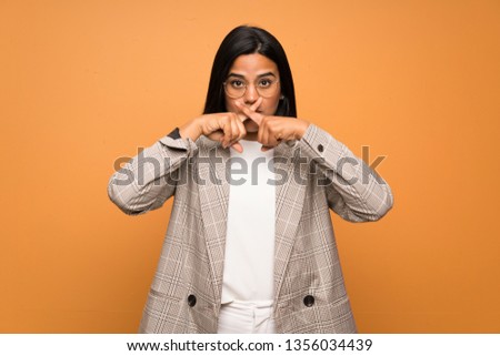 Young Colombian girl over brown wall showing a sign of silence gesture