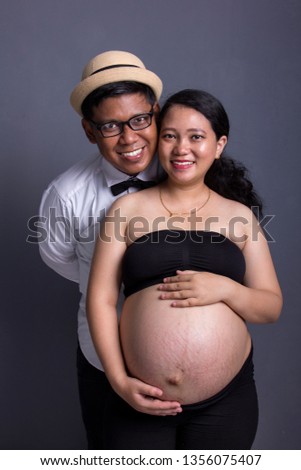 Portrait of happy smiling Asian family expecting baby birth, posing to camera, indoors maternity concept image